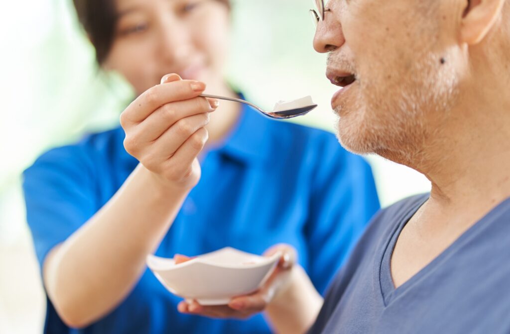 A care worker is feeding a senior resident some food in assisted living.