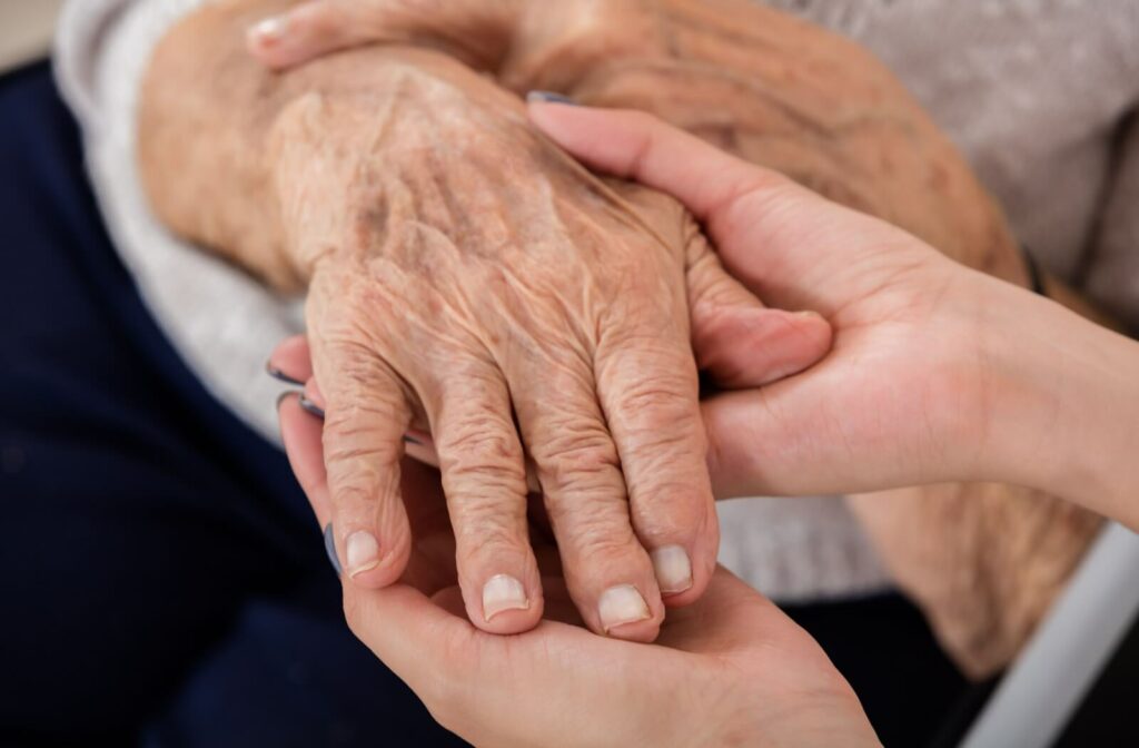 Close-up of a caregiver gently holding the hand of an older adult during a comforting moment