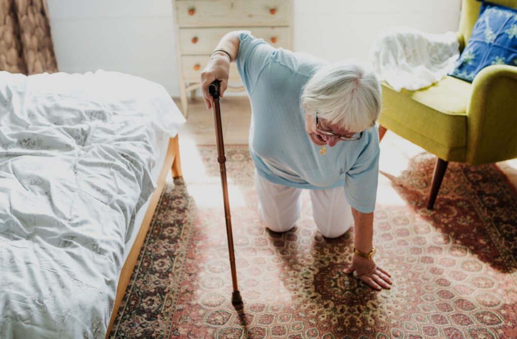 Older adult using a cane to rise from the floor after a fall beside a bed in a home setting