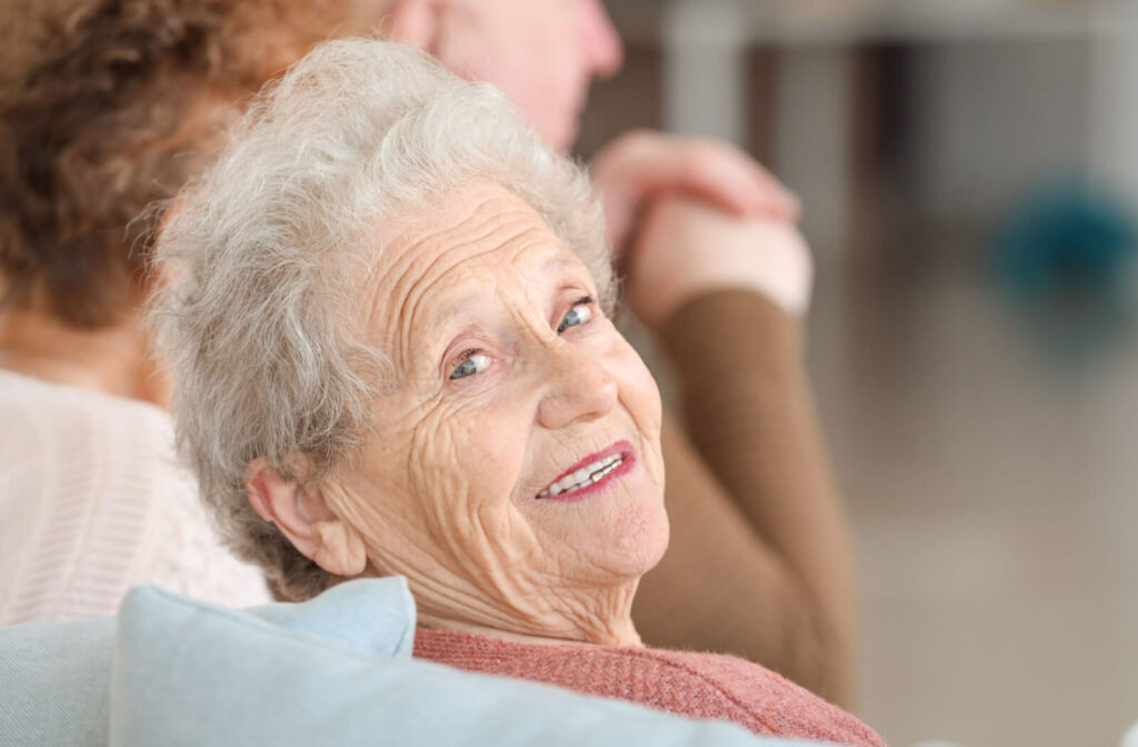 An older adult in assisted living turns to smile at the camera during a group activity.
