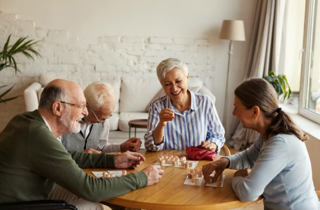 A group of four cheerful seniors are having fun sitting at a table and playing a bingo game in assisted living.