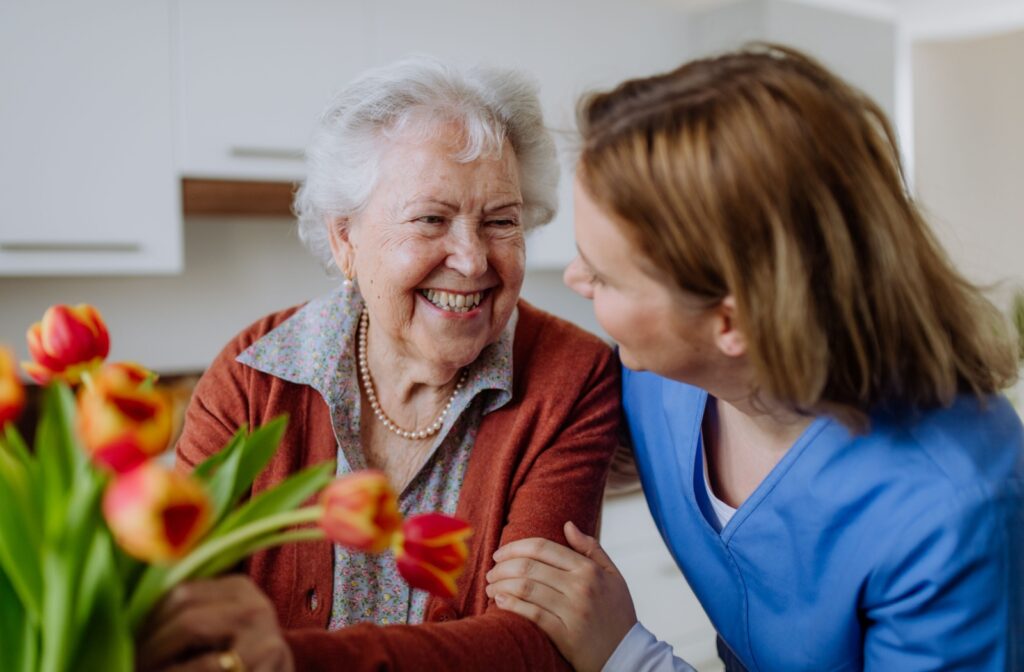 A senior and caregiver smile at each other in assisted living, with a tulip bouquet in the foreground.