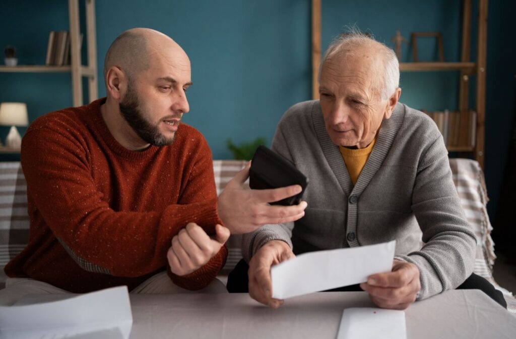 An adult child shows their older parent their cell phone while reviewing a budget together during an application for assisted living