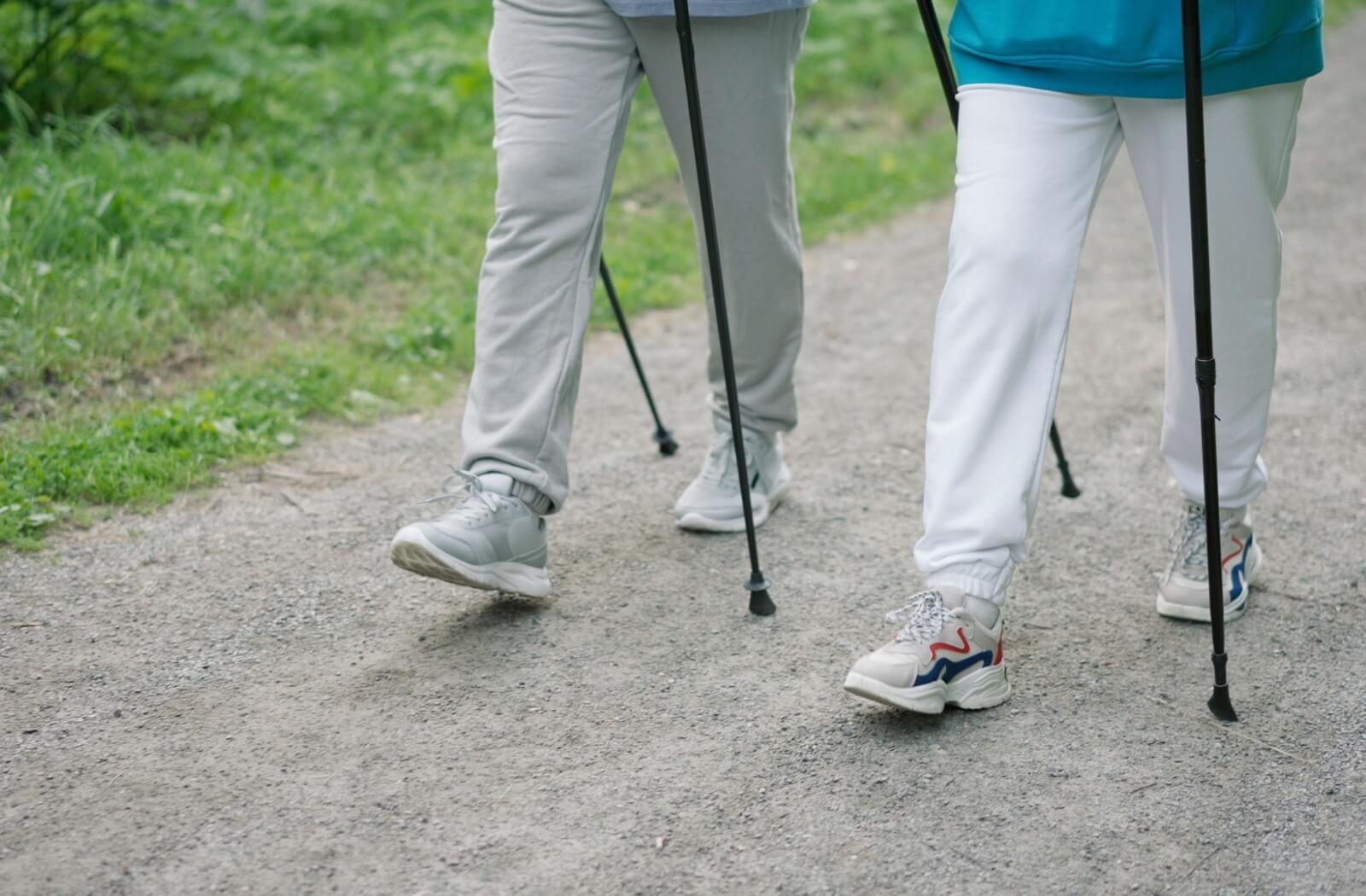 Two seniors walk together with the help of walking sticks.